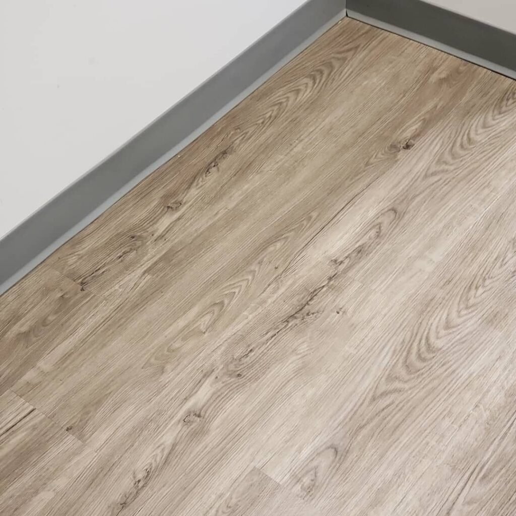 Close-up of a light wood-look plank floor with matching baseboard - Pi Floor & Blinds Victoria BC