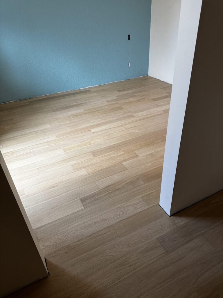Bedroom with a teal feature wall and new light plank flooring - Pi Floor & Blinds Victoria BC
