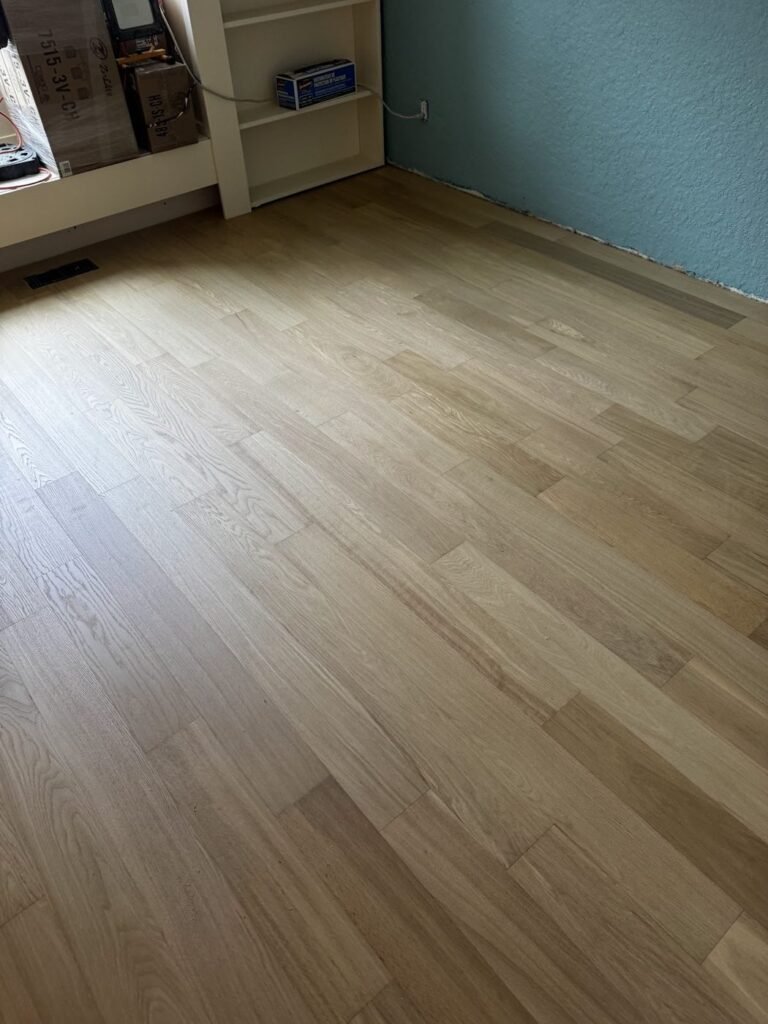 Room with a teal accent wall and honey oak plank flooring - Pi Floor & Blinds Victoria BC